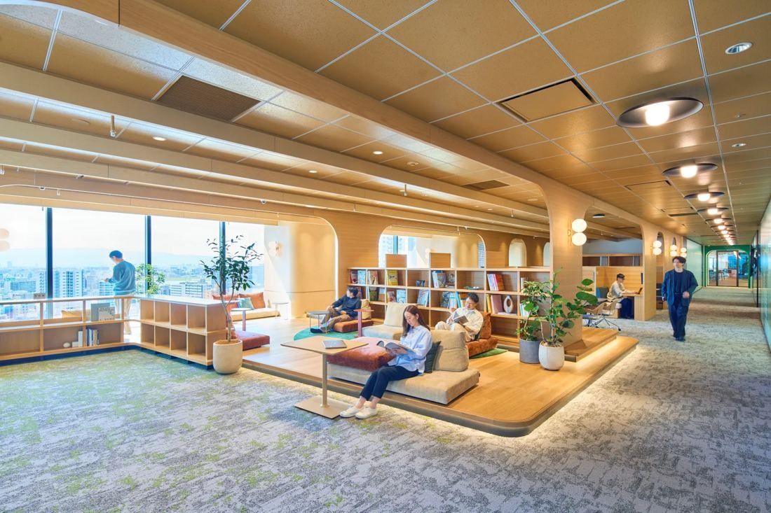 KOKUYO: Raised timber platform with cushions and bookshelves next to a window with a city view