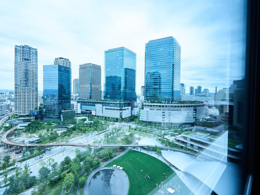 KOKUYO: View through a window over a park lawn and pond with glass towers behind