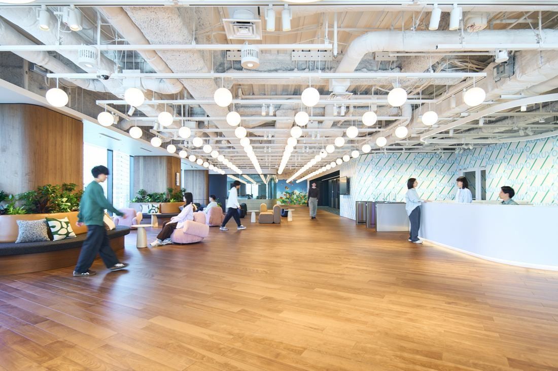 KOKUYO: Wide wood-floored entrance area with a white reception counter and pendant lights