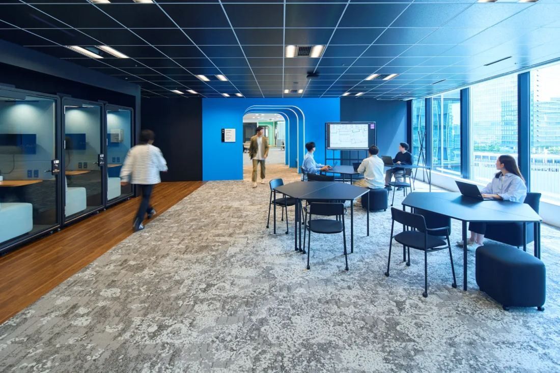 KOKUYO: Work area with round tables, phone booths along a wall and a blue arched doorway