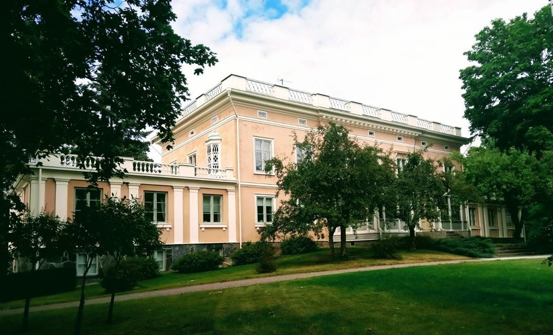 KONE: Long pale manor building behind trees and a green lawn