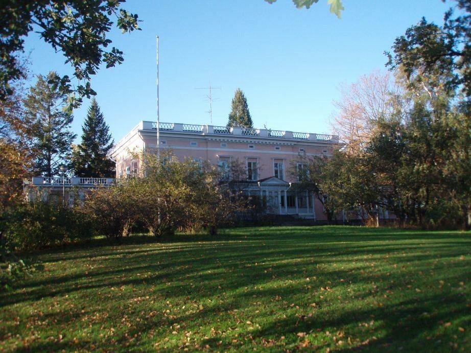 KONE: Manor house beyond a lawn and fruit trees in low sunlight