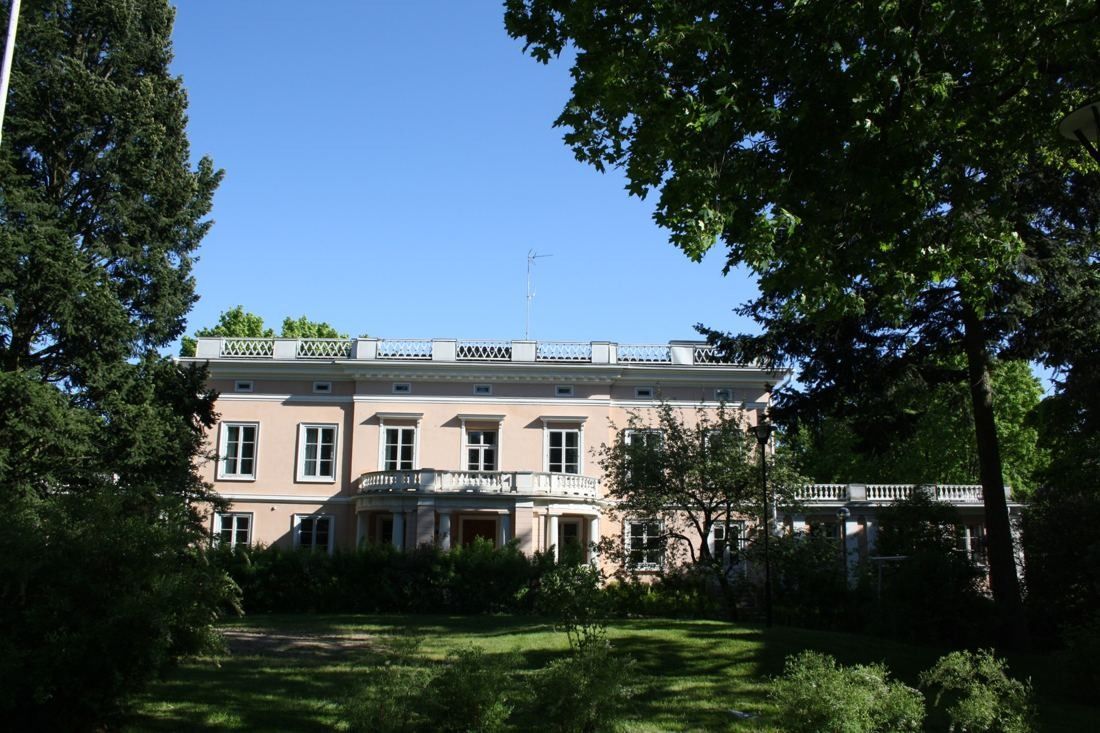 KONE: Manor house glimpsed through trees beyond a shaded garden
