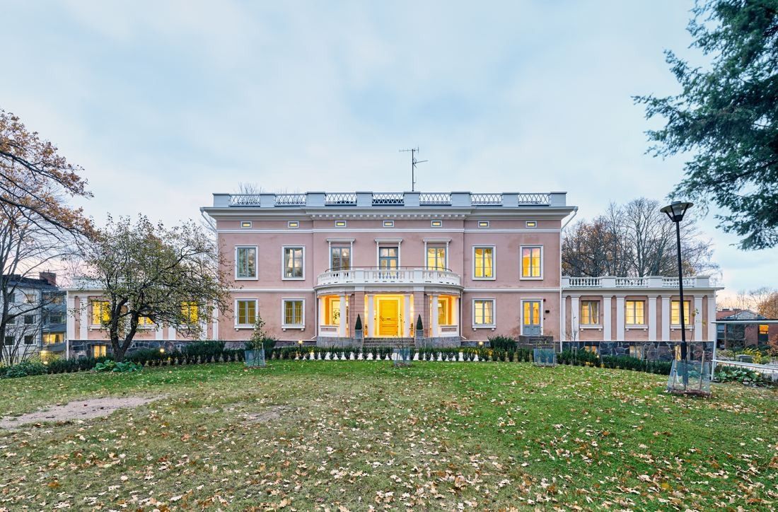 KONE: Pink manor house with lit windows seen across a wide lawn in autumn