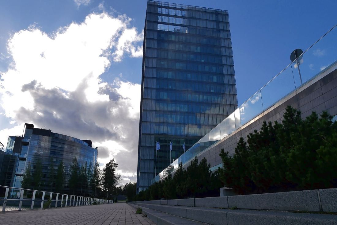 Slim glass tower rising beside a paved waterfront walkway under a cloudy sky