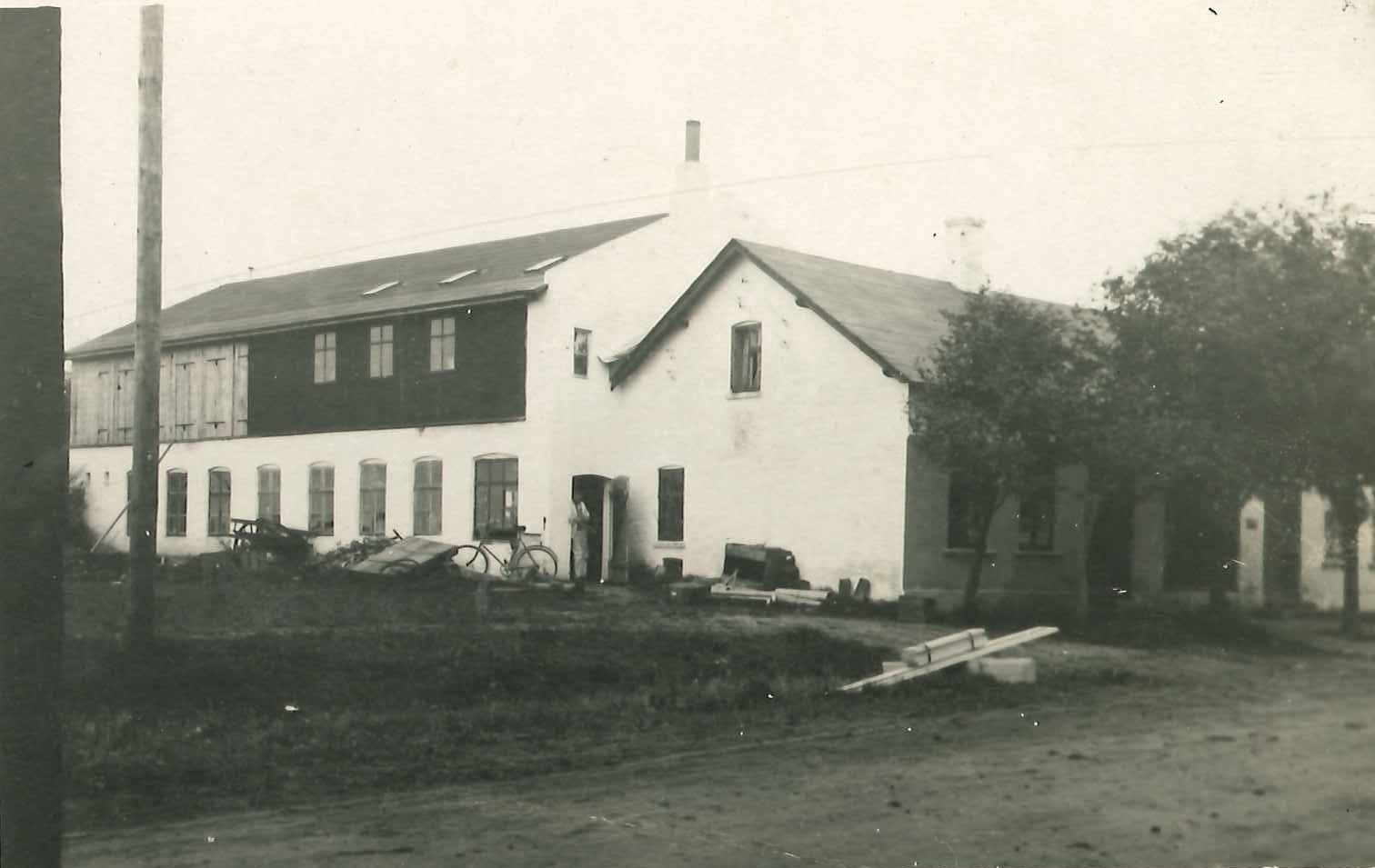 Sepia photo of a long white two-storey house and workshop beside a dirt road