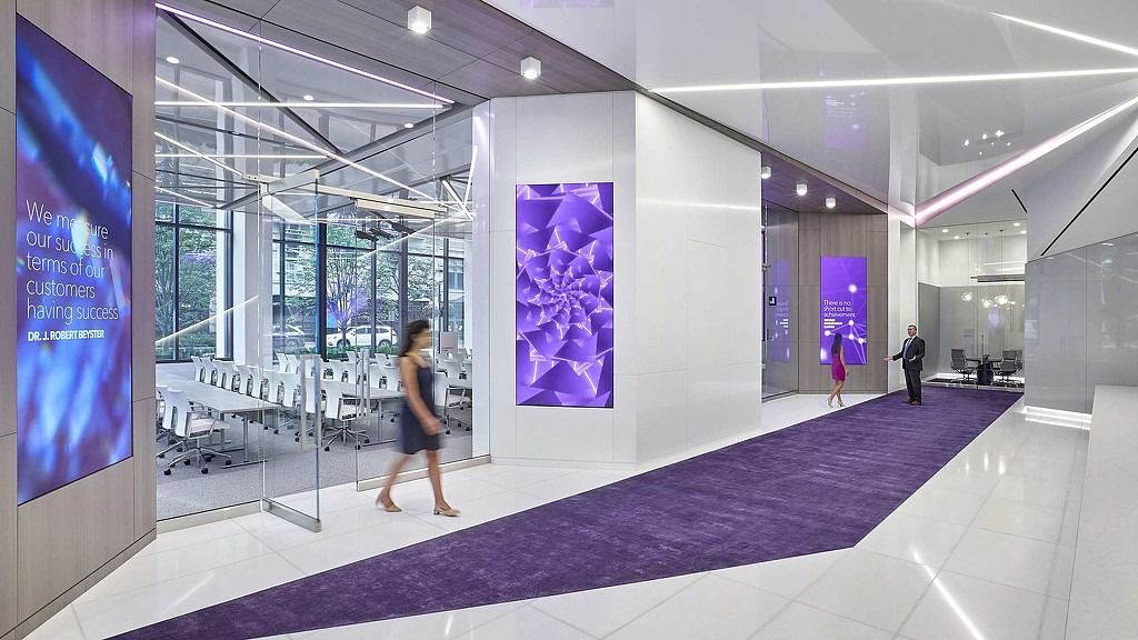 A white lobby with a purple runner, glass walls and glowing purple art panels