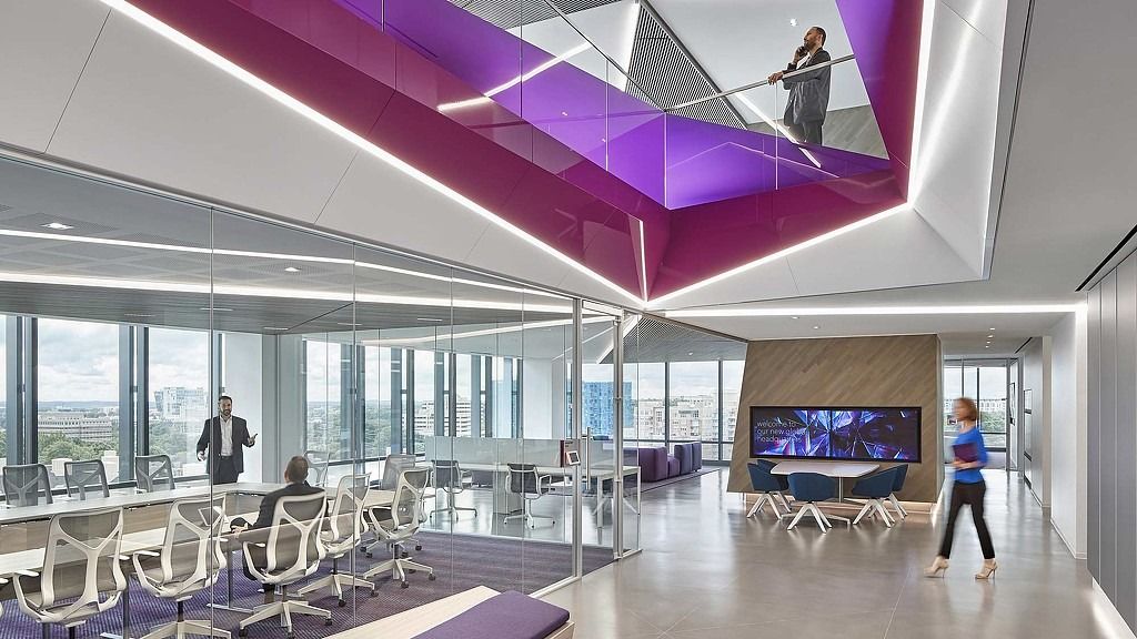 Leidos: An open office under a double-height opening with a purple ceiling and people on the floor above