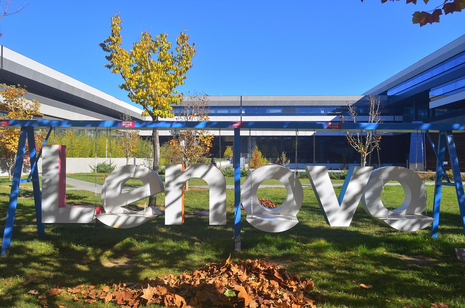 Large silver Lenovo letters on a lawn in front of a long glass building