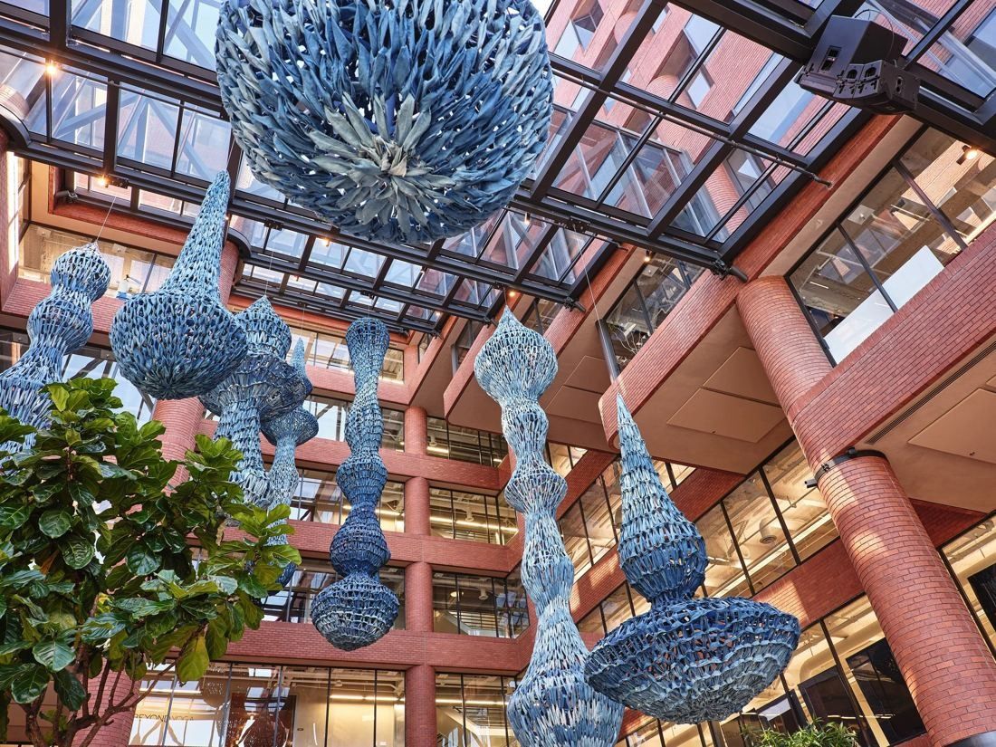 Levi Strauss & Co.: Looking up through the atrium at blue woven sculptures hanging below a glass roof between brick columns