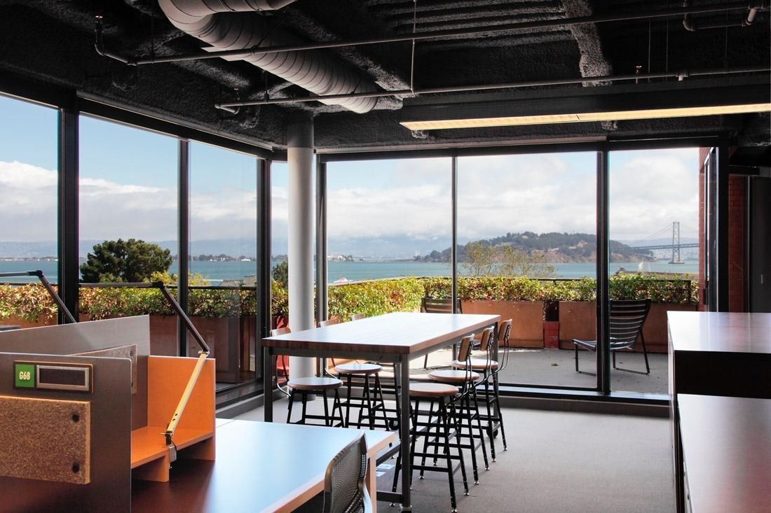 Levi Strauss & Co.: Office floor with tall tables and a glass wall opening onto a terrace with a view of the bay and a bridge