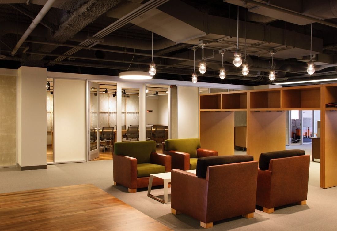 Levi Strauss & Co.: Open lounge with leather armchairs, pendant lights and wooden shelving in an office with exposed ceiling