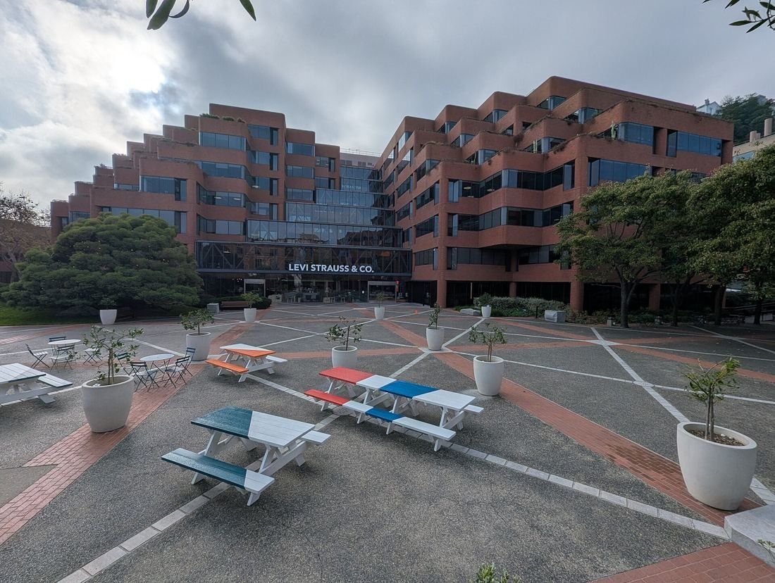 Levi Strauss & Co.: Stepped red-brick office building with a paved plaza and picnic tables in front