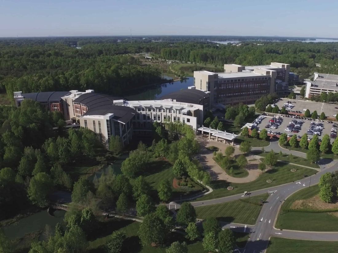 Lowe's: Aerial view of a wooded campus with large office buildings, a lake, parking and curving roads
