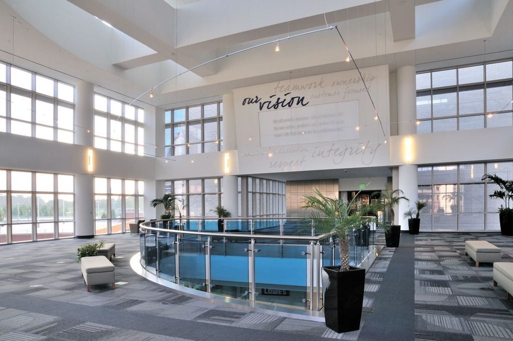 Lowe's: Bright double-height atrium with tall windows, a curved glass railing, potted palms and seating