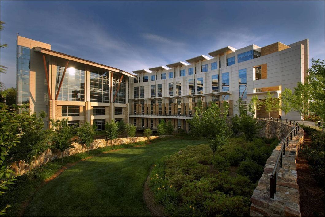 Lowe's: Long multi-storey office building with stone walls and a planted garden in the foreground at dusk