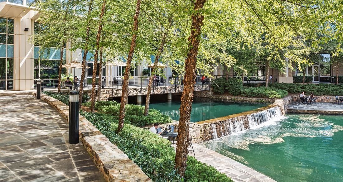 Lowe's: Stone path under trees beside a small waterfall flowing into a pool next to office buildings
