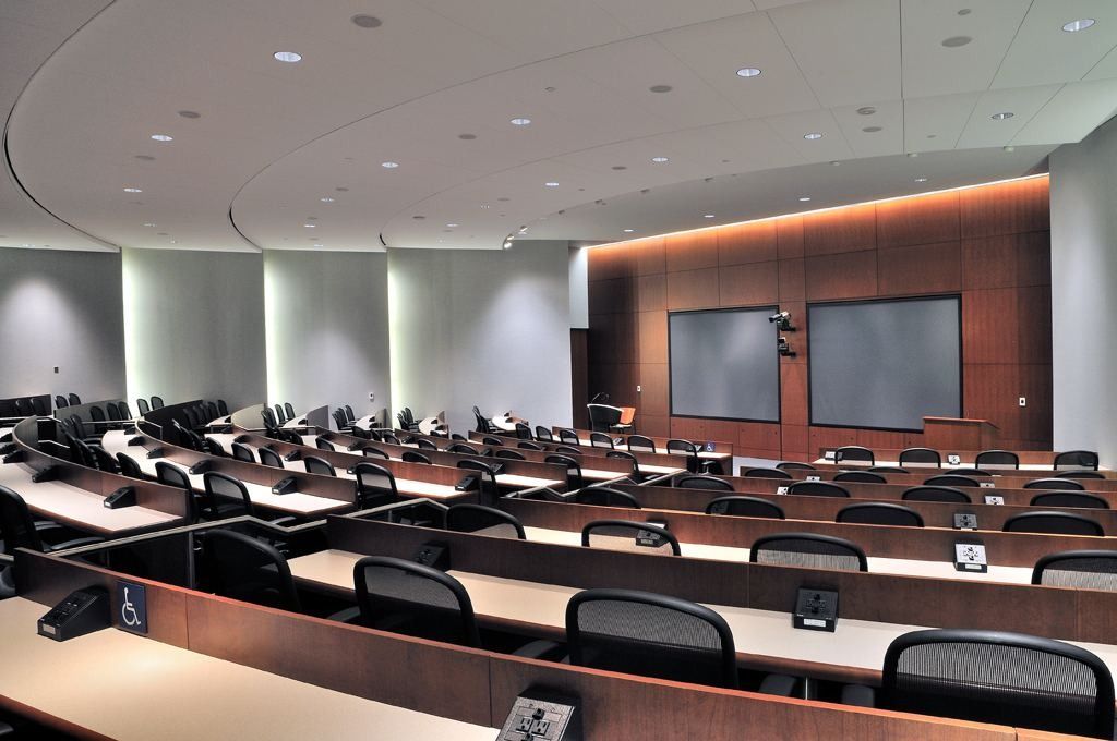 Lowe's: Tiered auditorium with curved desks, chairs and two screens on a wood-panelled wall