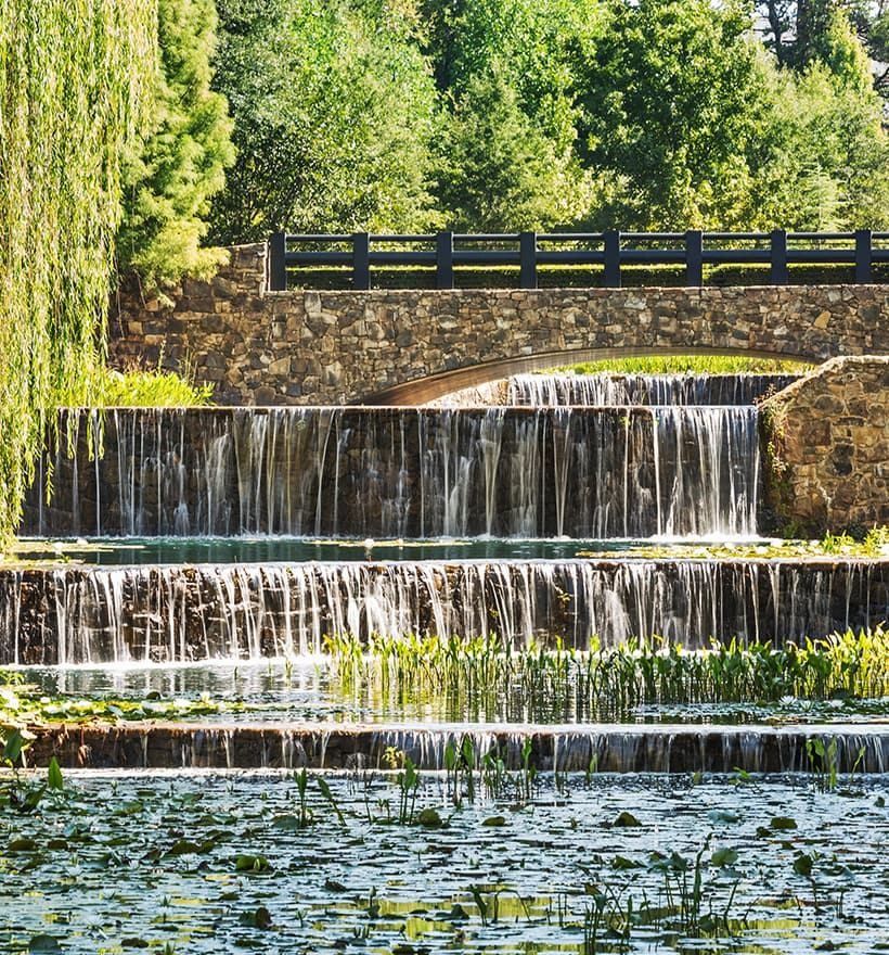 Lowe's: Tiered stone waterfalls cascading into a pond with lily pads, a railing above