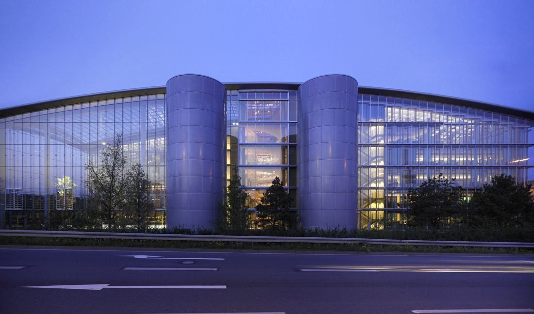Lufthansa Group: Glass building with two round towers in front, lit at dusk beside a road
