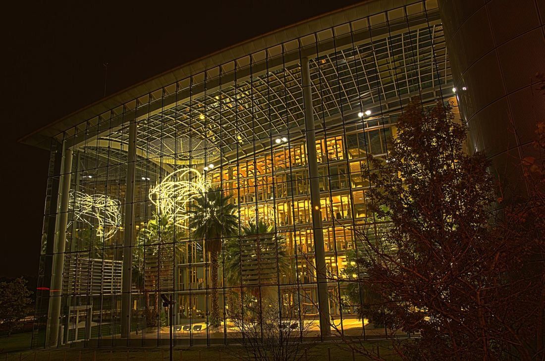 Lufthansa Group: Large glass end wall of a garden hall at night with palms and a light sculpture