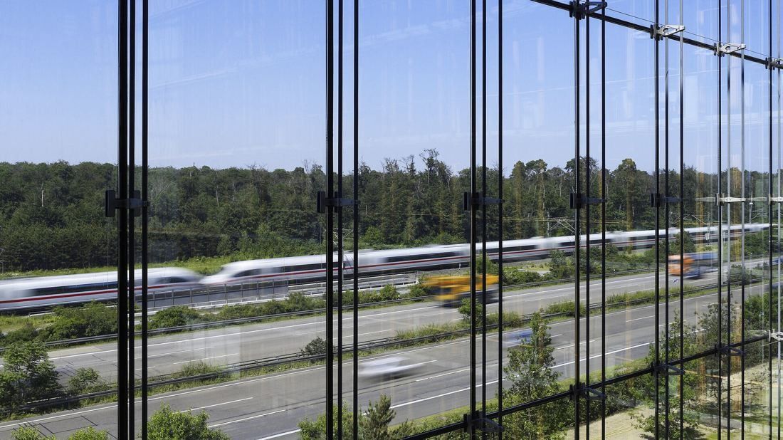 Lufthansa Group: View through a glass facade onto a motorway and a passing high-speed train