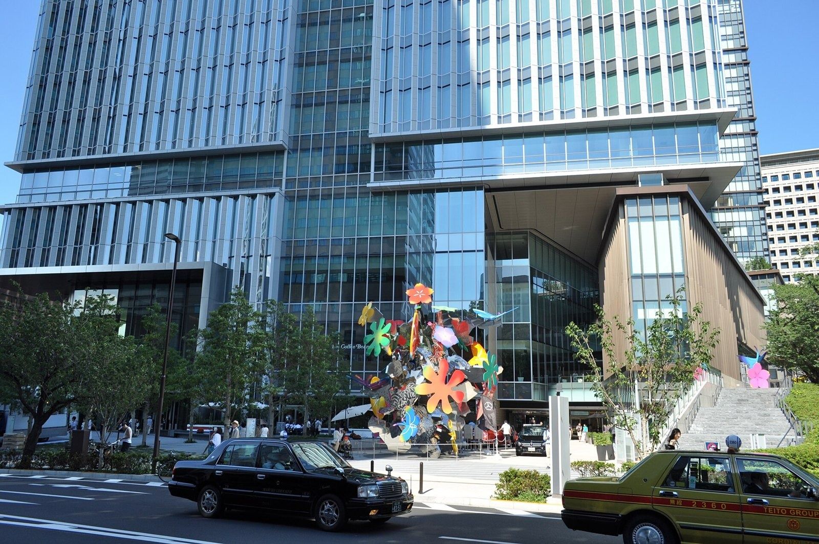 LY Corporation: Base of a glass tower with a colourful flower sculpture and taxis in front