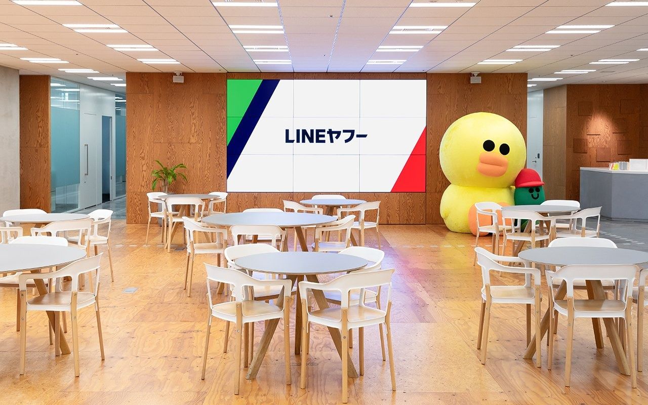 LY Corporation: Café tables in front of a large screen and a big yellow character figure