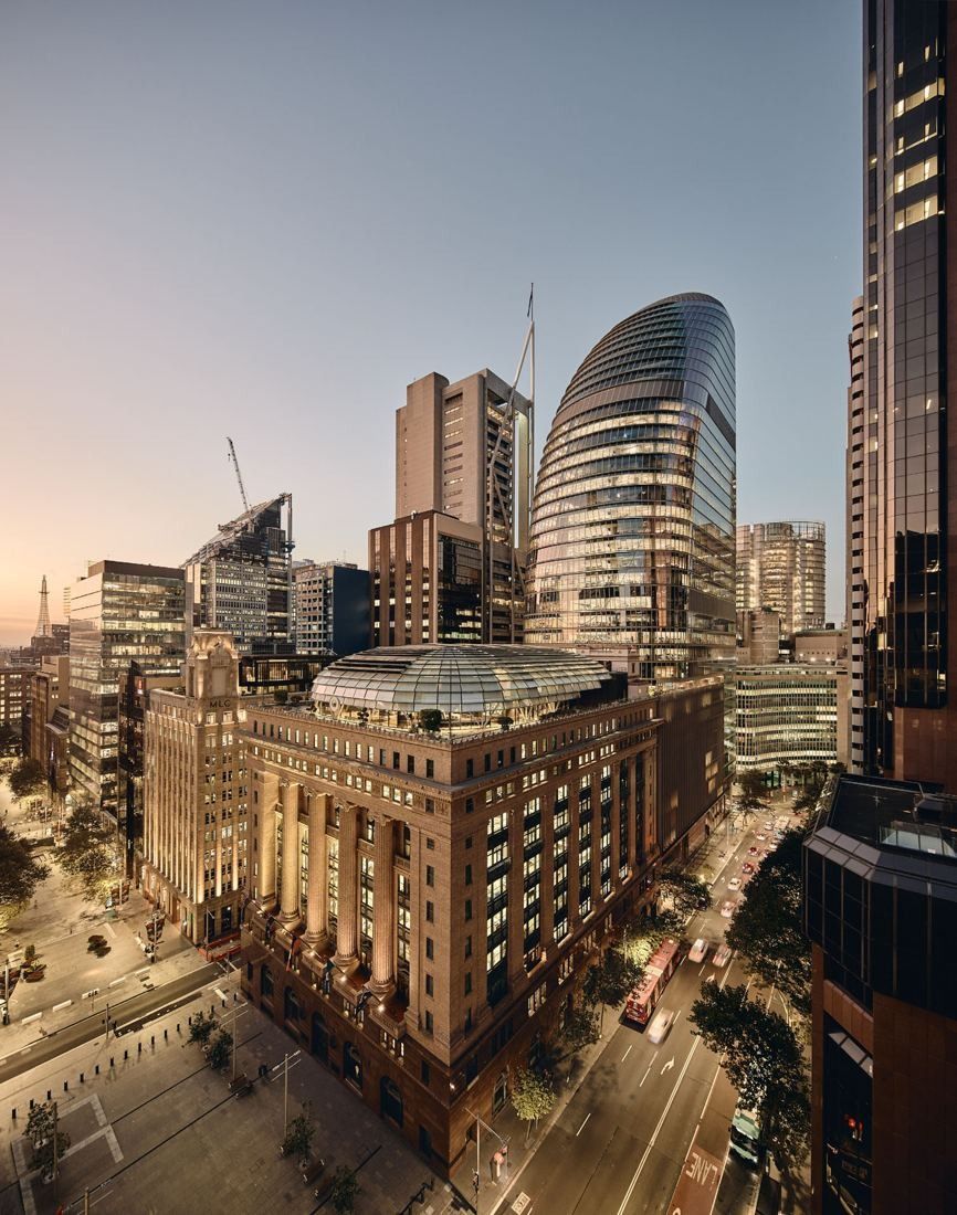 Macquarie Group: Glass tower rising behind a sandstone bank building at sunset