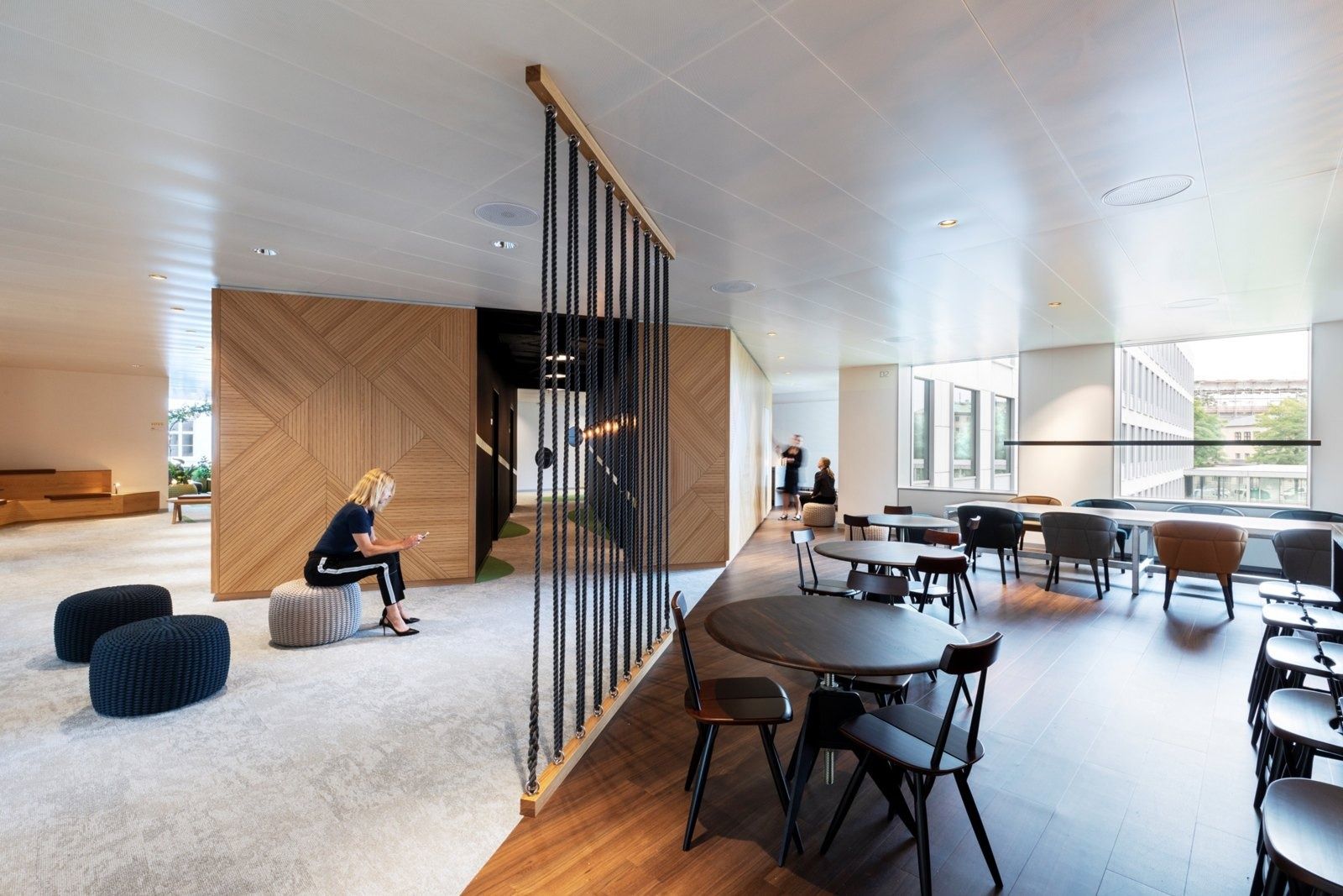 A.P. Moller - Maersk: Bright lounge with knitted poufs, a rope screen, oak-panelled walls and café tables by the windows
