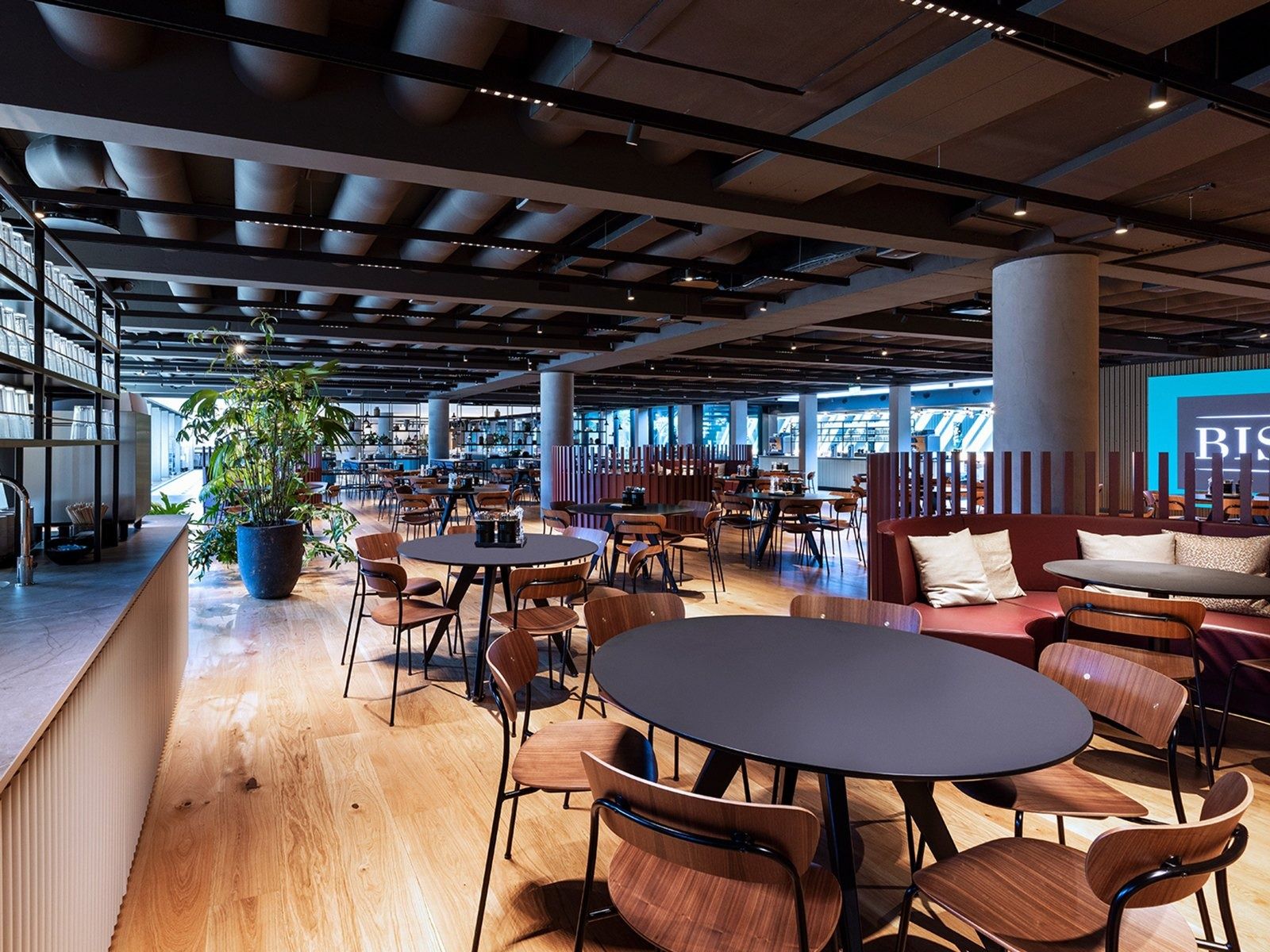 A.P. Moller - Maersk: Dining area with round black tables, wooden chairs, a red banquette and a long window wall