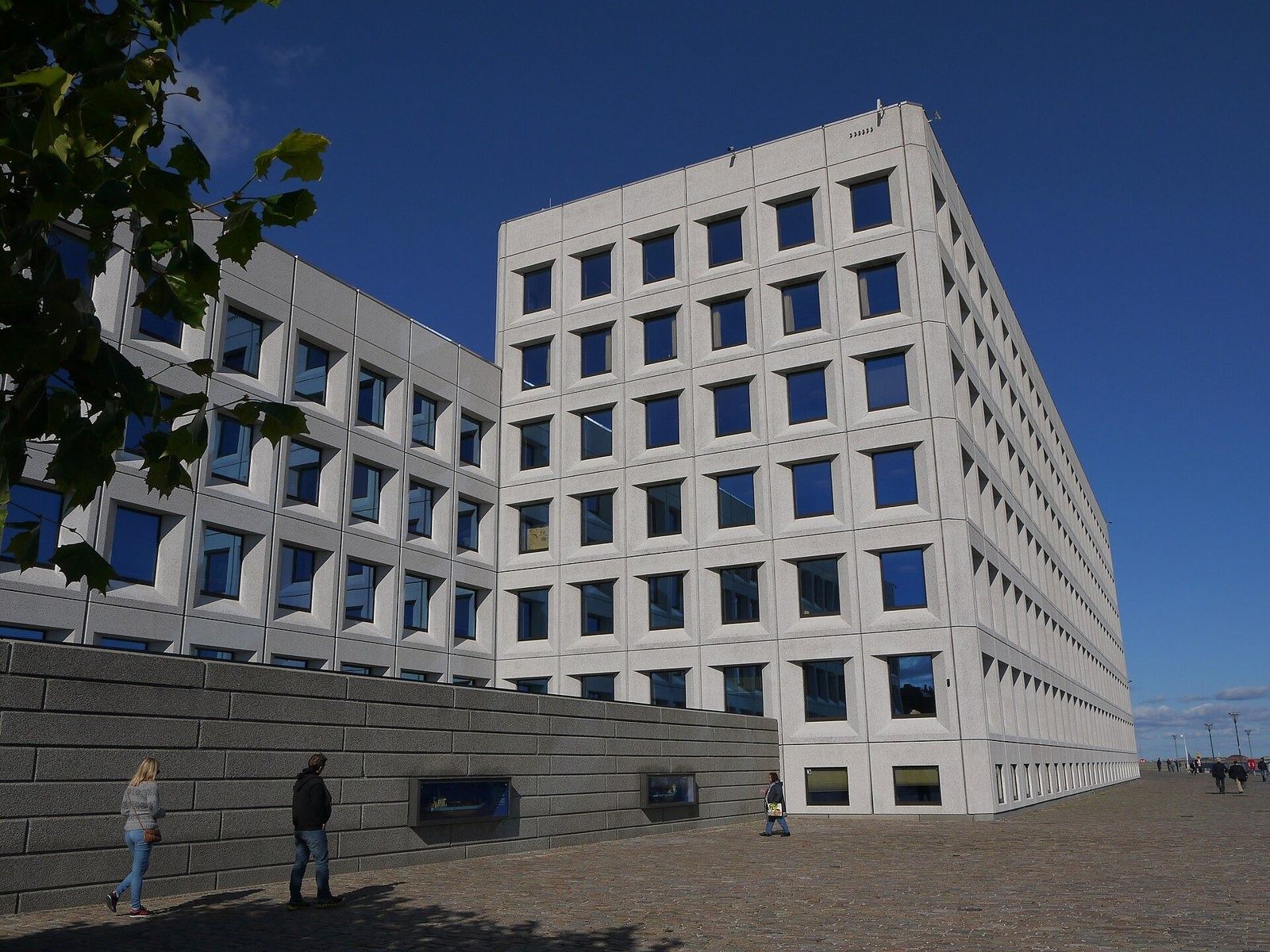 A.P. Moller - Maersk: Pale concrete building with deep-set square windows seen from a low angle on a paved quay