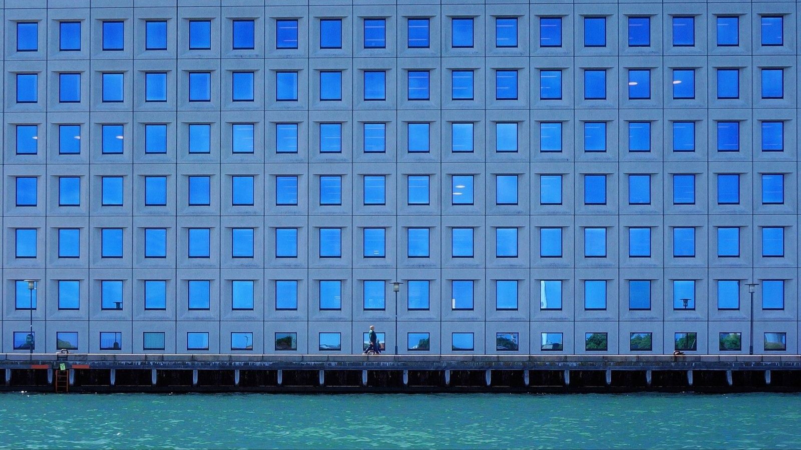 A.P. Moller - Maersk: Straight-on view of a facade grid of square windows reflecting blue sky, above the water