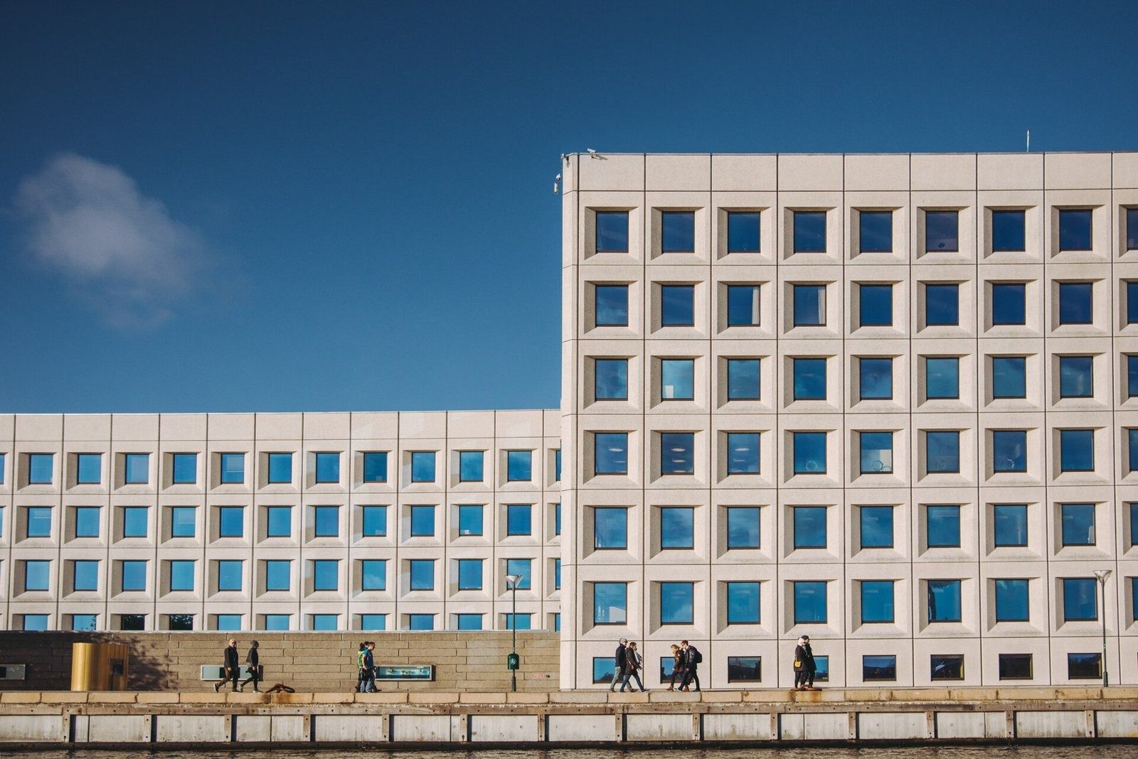 A.P. Moller - Maersk: Tall block with square windows beside a lower wing, people walking on the quay below