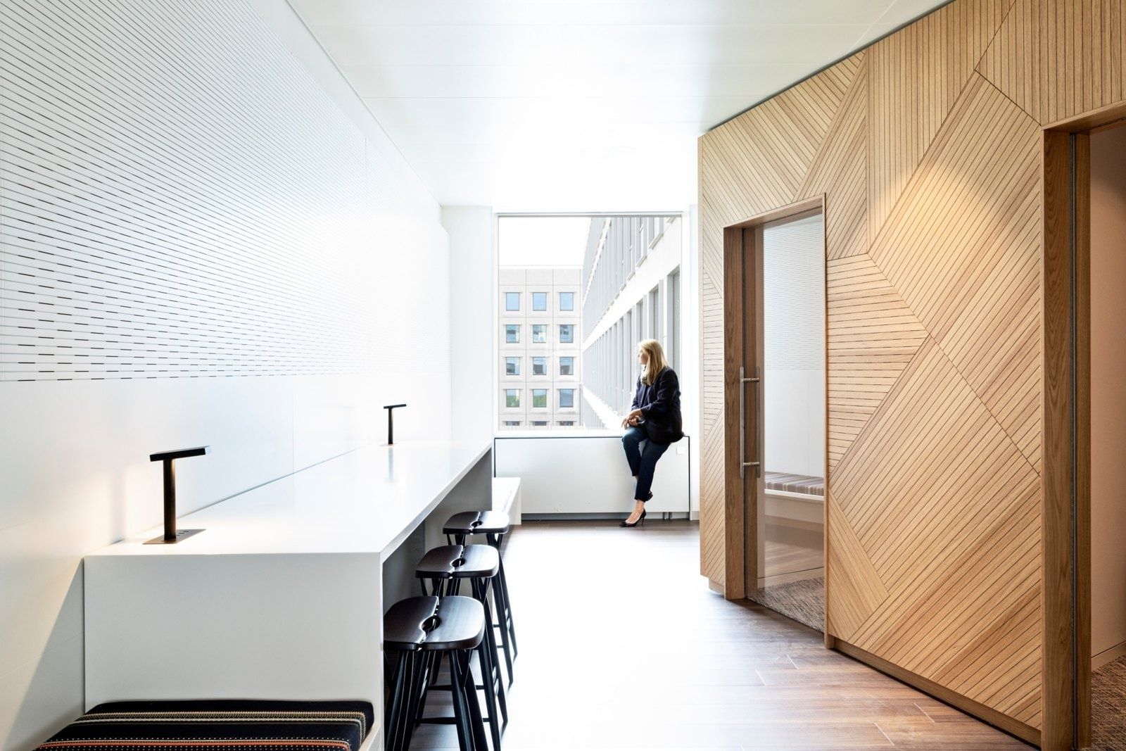 A.P. Moller - Maersk: White standing counter with bar stools beside oak-panelled walls and a window onto the courtyard facade