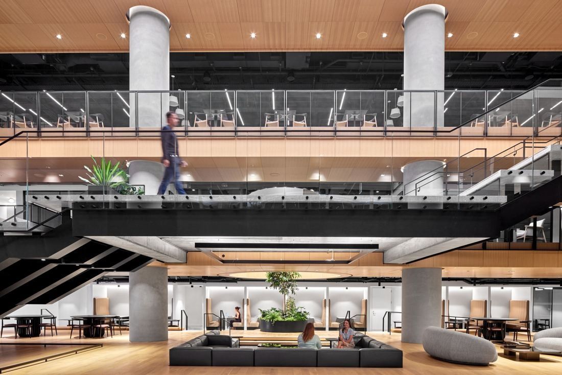 Marriott International: Bridge and stairs crossing an atrium above a sunken lounge with a planted tree and booth seating