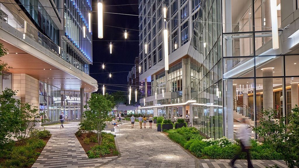 Marriott International: Landscaped pedestrian plaza at night between glass towers, lit by hanging pendant lights