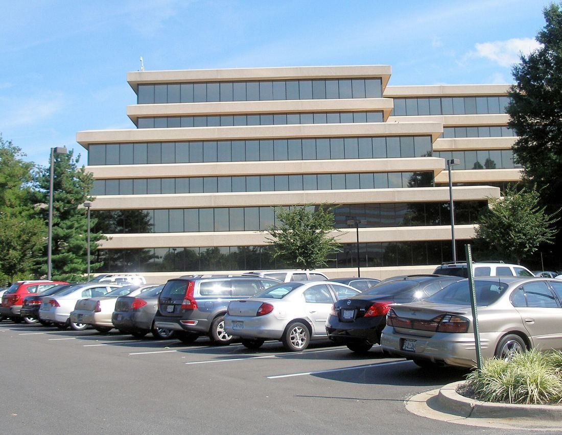 Low terraced office building with horizontal bands behind a parking lot