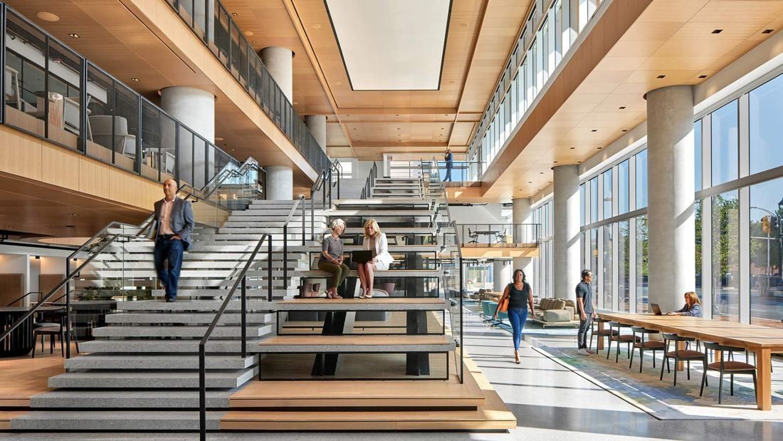 Marriott International: Wide stone-and-wood staircase rising through a multi-storey atrium with tall windows and a long wooden table