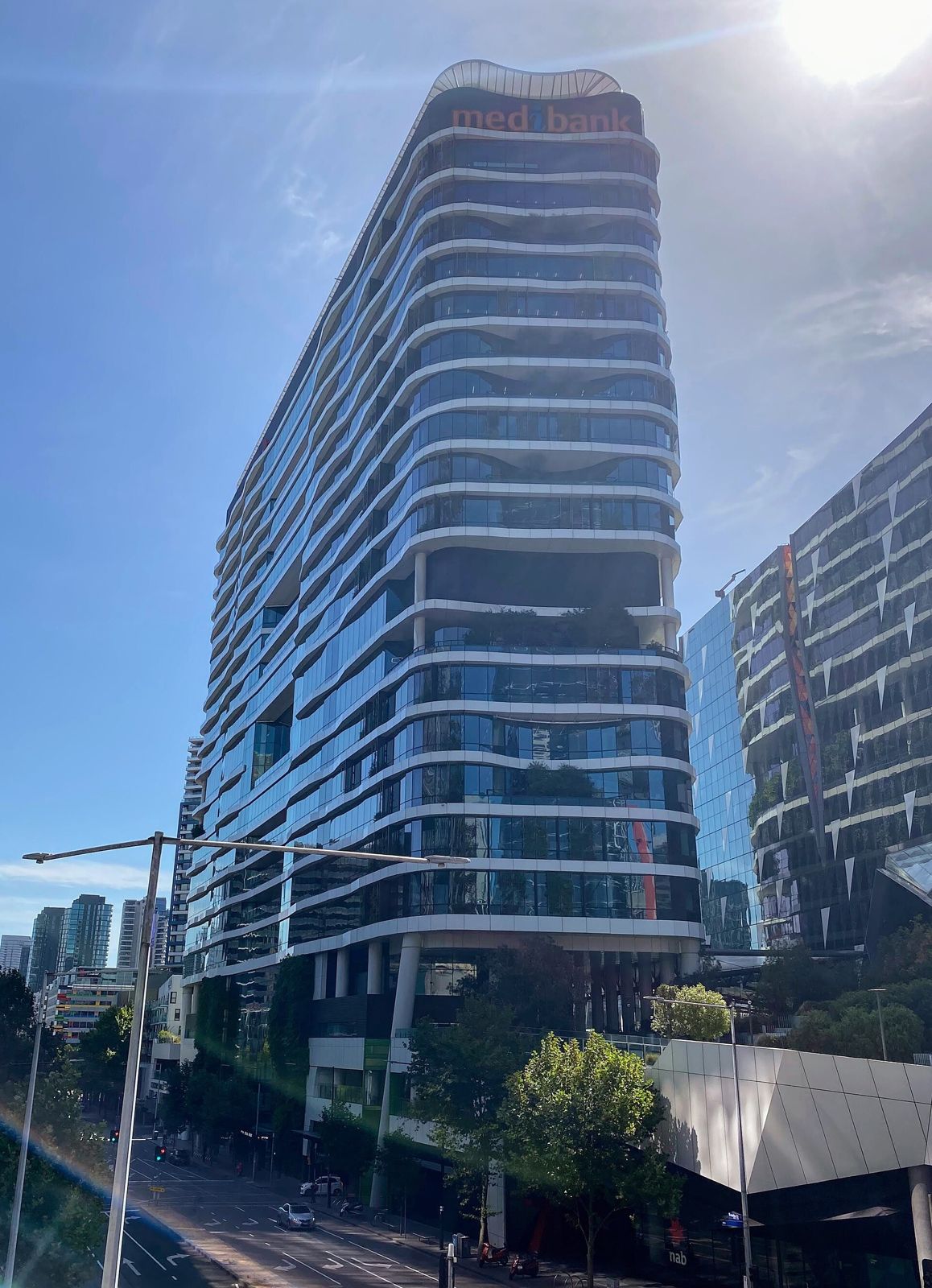 Medibank: A curving glass tower with plants on its balconies seen from the street