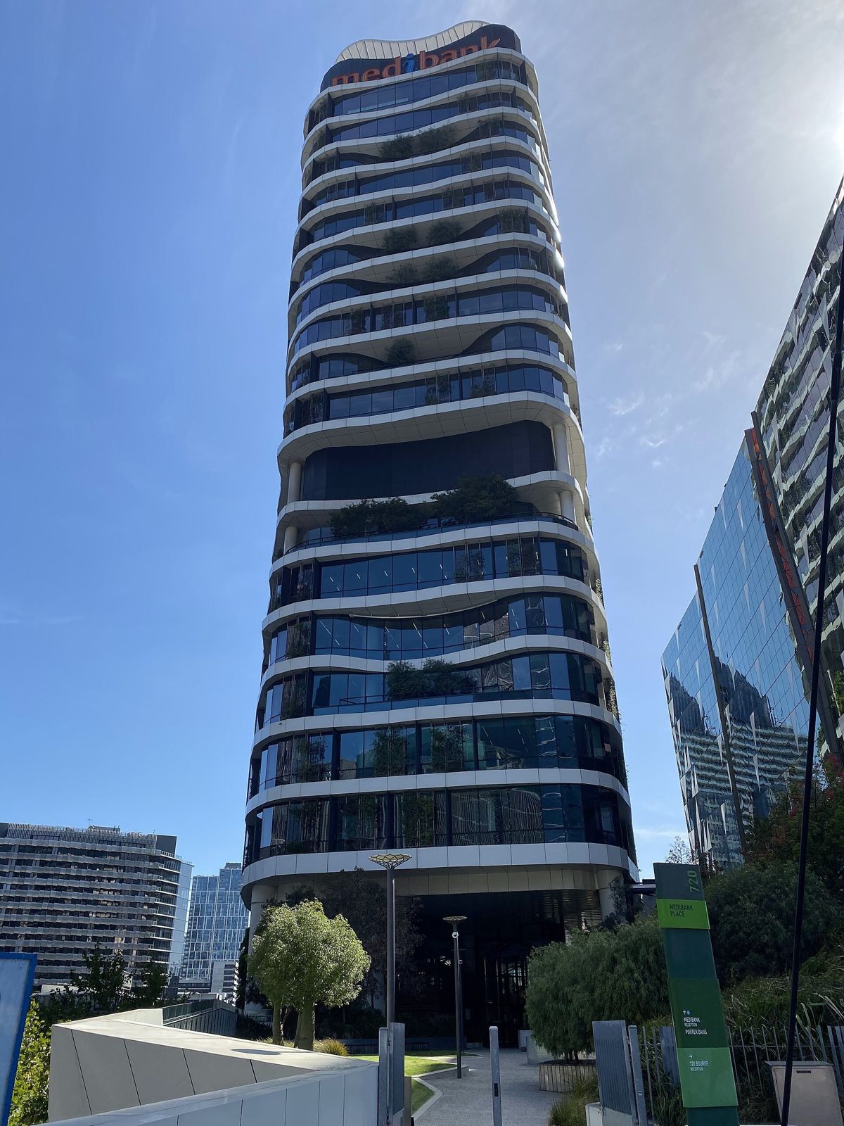 Medibank: A slim glass tower with wavy white floor bands against a blue sky