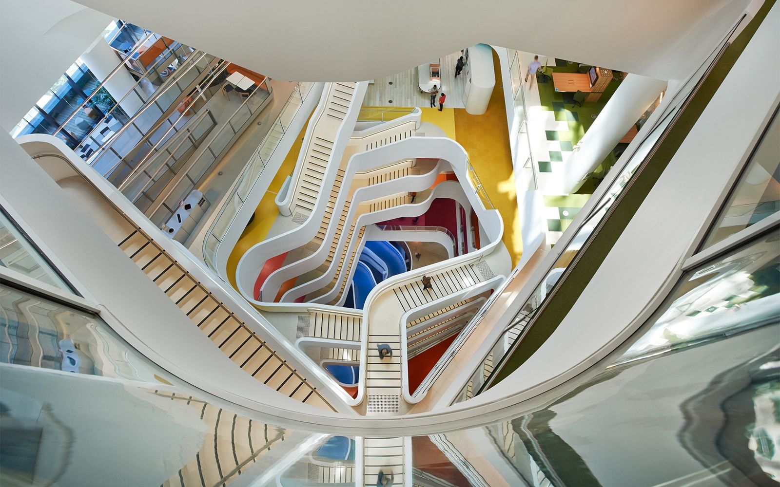Looking up through a tall atrium of white curving stairs with yellow, red and blue floors
