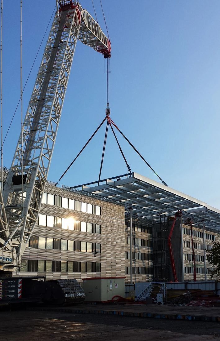 A crane lifting a large roof element above an office building under construction
