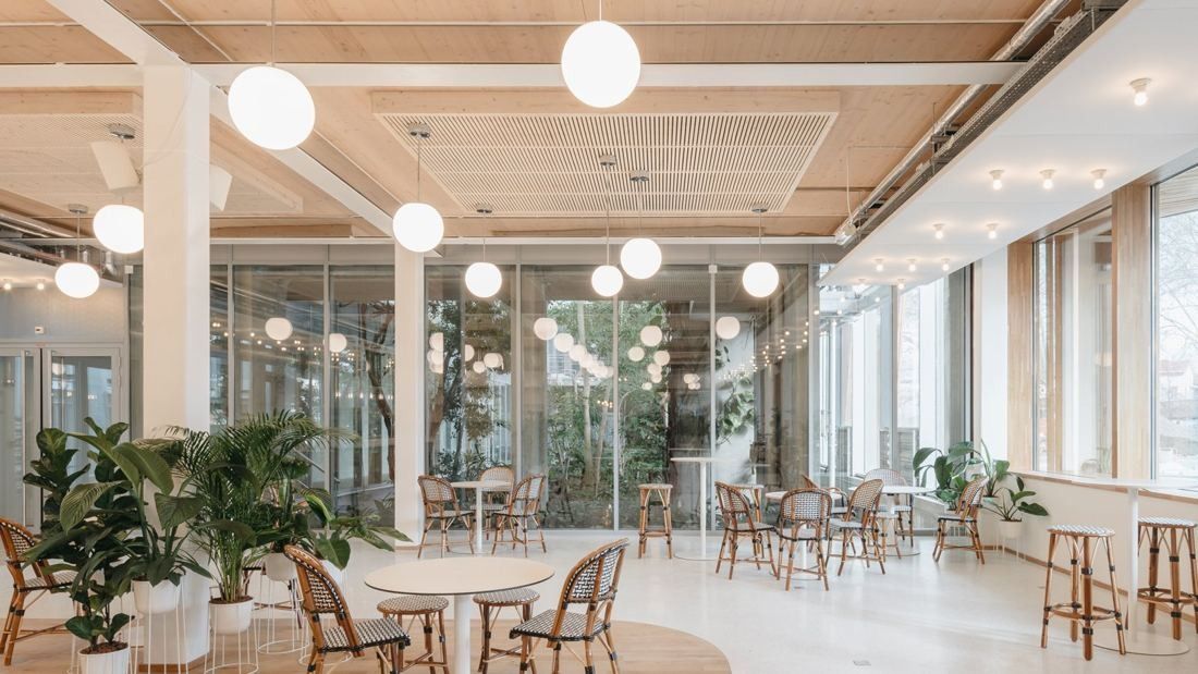 Michelin: Café with round tables, rattan chairs, globe lights and plants, with glazing onto a planted space