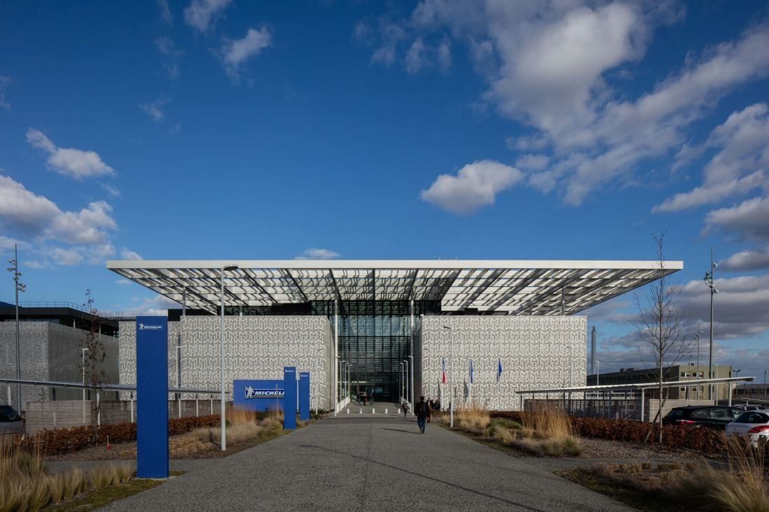 Michelin: Long building with a large flat canopy roof at the end of a straight path, under a blue sky