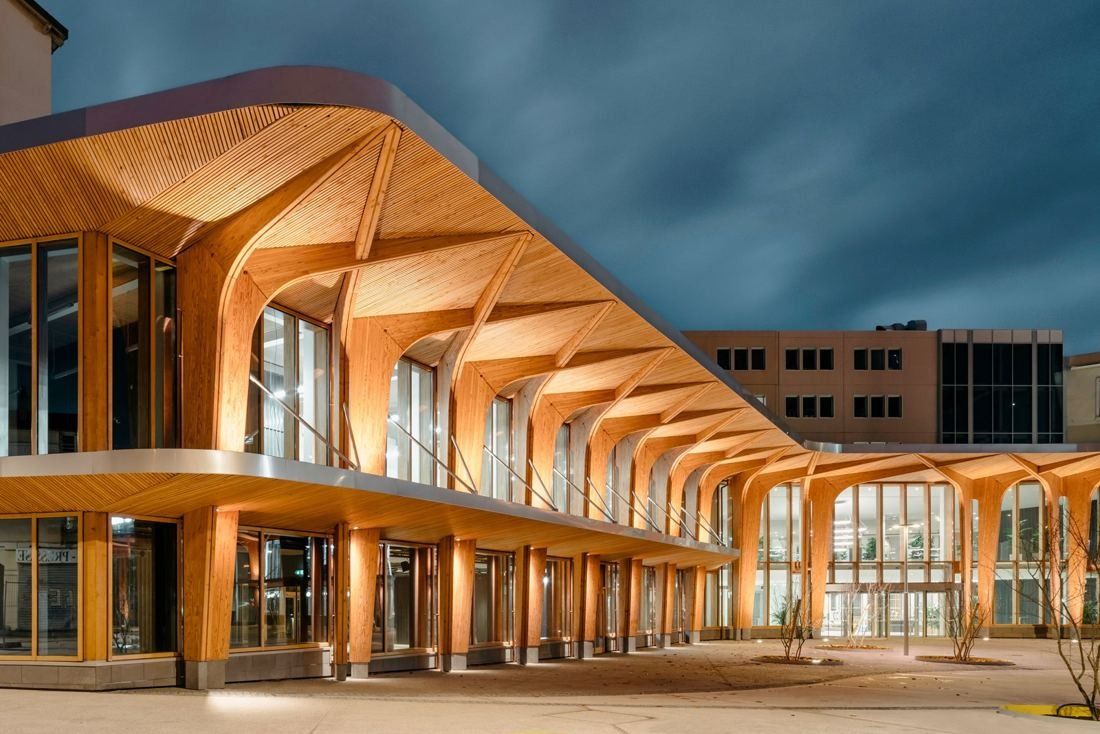 Michelin: Long timber canopy with branching wooden columns along a glazed ground floor at dusk