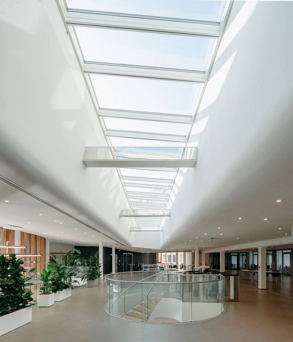 Michelin: Long white corridor under a continuous skylight with plants and a glass balustrade