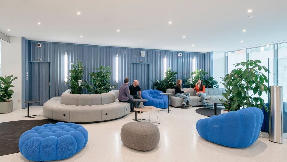 Michelin: Lounge with a curving grey sofa, blue armchairs and plants against a blue ribbed wall
