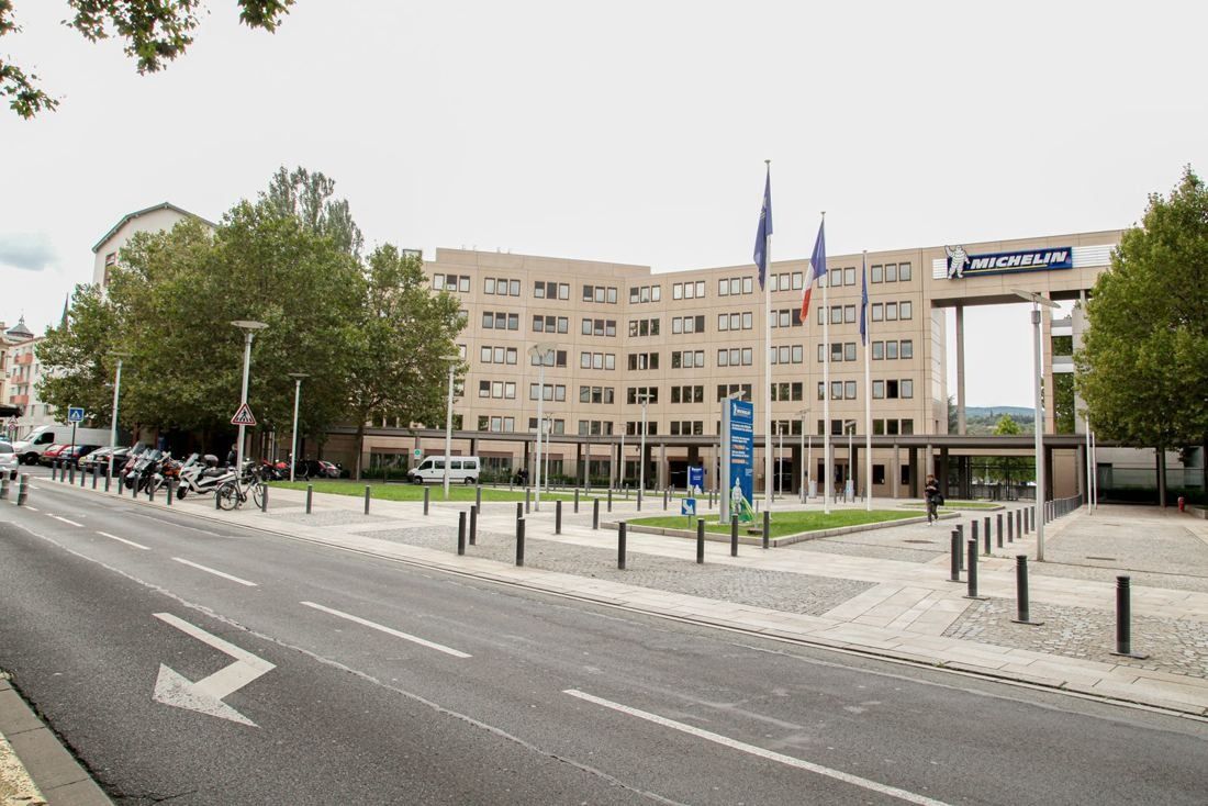 Michelin: Older multi-storey headquarters building with flags behind lawns and a city street