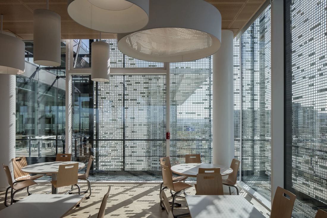 Michelin: Seating area with round tables under large drum lights beside a perforated façade